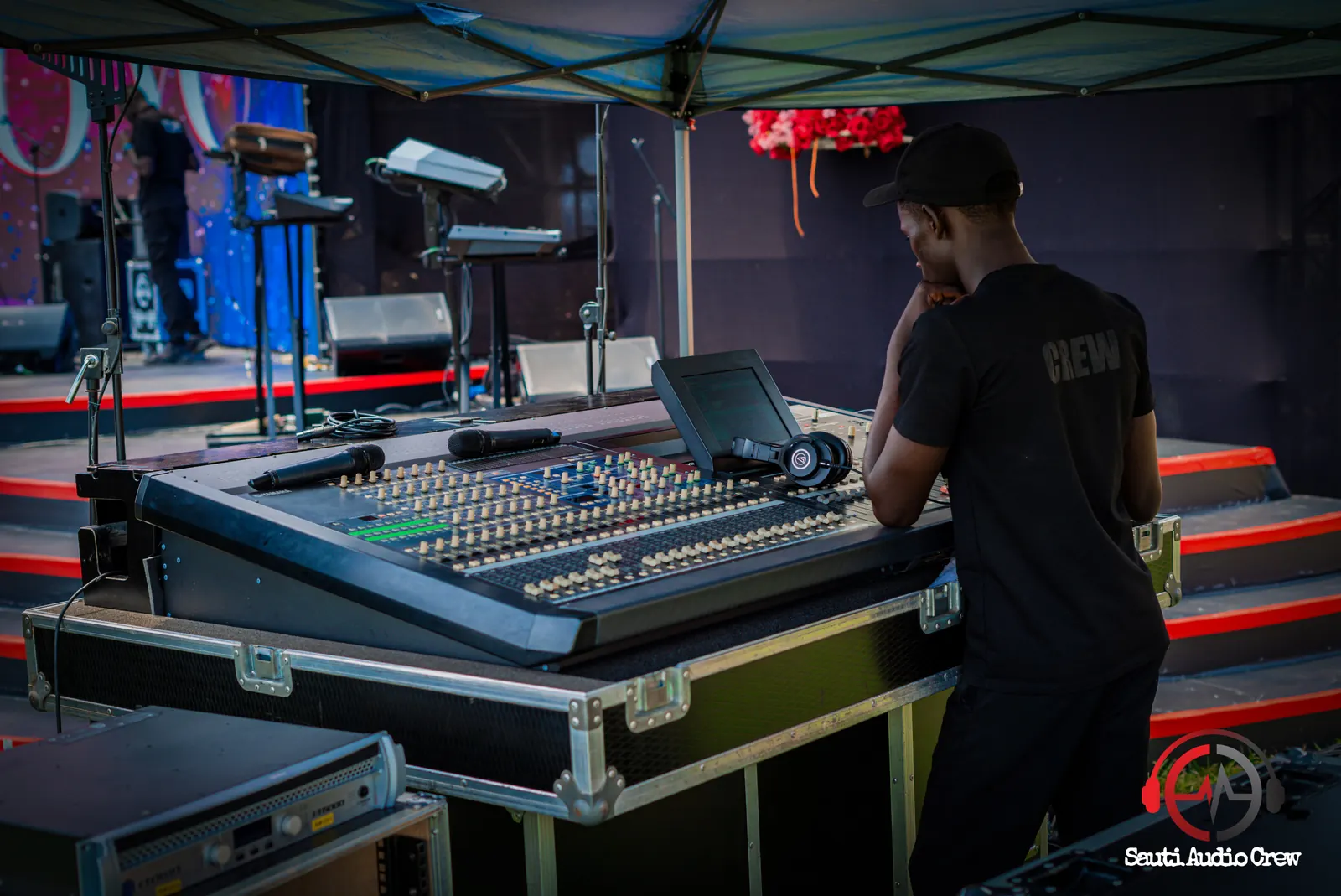 Sauti engineer at a digital mixing console beside the stage
